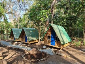 three huts with green roofs in a forest at MoRue's Den in Mabini