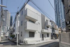 ein weißes Gebäude in einer Stadtstraße mit hohen Gebäuden in der Unterkunft Felice Nishi-Shinjuku in Tokio