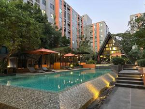 a swimming pool with chairs and umbrellas next to buildings at Cozy,convenient,shopping area in Chiang Mai