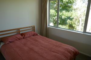 uma cama com um edredão vermelho em frente a uma janela em The Tree house em Paraparaumu