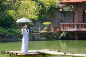 une femme debout sur un radeau avec un parapluie dans l'établissement Khu du lịch sinh thái Cỏ Lau Village, à Làng Song Ca