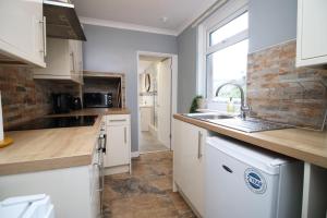 eine Küche mit weißen Schränken, einem Waschbecken und einem Fenster in der Unterkunft Cosy 3BR Home, Scenic Views, Ideal for Walks & Work in Abertillery