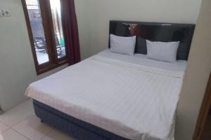 - un lit avec des draps et des oreillers blancs à côté d'une fenêtre dans l'établissement SPOT ON 93815 Chimi Rumah Kost, à Purwokerto