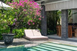 a chair next to a swimming pool with pink flowers at Villa Minha Gente Seminyak in Seminyak