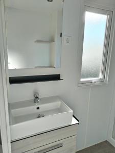 a white bathroom with a sink and a window at Camping Le Lac des Rêves Lattes in Pérols