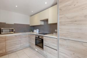 a kitchen with wooden cabinets and a microwave at Modern Two Bedrooms Flat in Kingston KT2, London in Kingston upon Thames