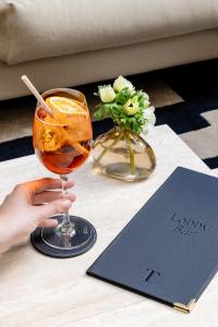 a person holding a drink on a table with a book at TÓTEM Madrid, a Small Luxury Hotel of the World in Madrid