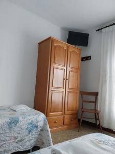 1 dormitorio con armario de madera, 1 cama y 1 silla en Pensión Glorioso Hostel, en Picaraña