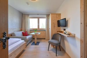 Habitación pequeña con cama, sofá y TV. en Pension Heim en Seeg