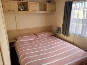 Schlafzimmer mit einem Bett mit rosa Bettwäsche und einem Fenster in der Unterkunft Caravan Sleeps 4 with Free Parking in Burnham on Sea