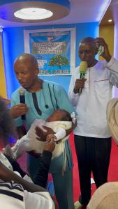 un homme tenant un bébé tout en tenant un microphone dans l'établissement Lakewood city Resort, à Narok