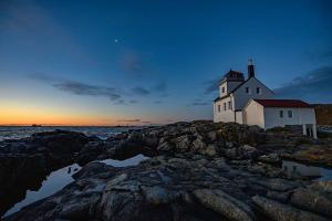 a lighthouse on a rocky shoreline at sunset at Lofoten Fyr in Værøy