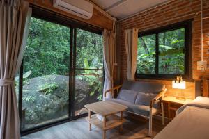a living room with a couch and large windows at Bee Forest in Ban Pok Nai