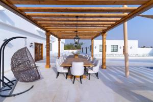 une salle à manger extérieure avec une table en bois et des chaises blanches dans l'établissement AL JUNAIDI FARM BY BRIDGE RETREATS, à Charjah