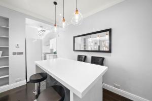 a white kitchen with a white counter and black chairs at South Kensington Luxury Suite in London