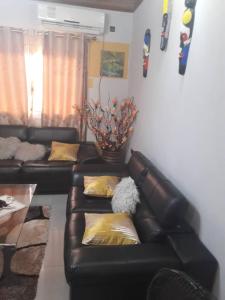 a living room with a black leather couch with yellow pillows at appartement meublé à Yansoki douala in Ngori