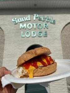 een persoon met een bord met een broodje erop bij Sand Pebble Motor Lodge in Point Pleasant Beach