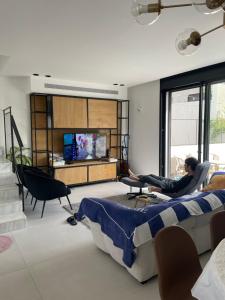 a man sitting on a couch in a living room watching tv at Aloni House In Dagan in Even Yehuda