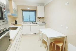eine weiße Küche mit einem weißen Tisch und einem Fenster in der Unterkunft T2 Sesimbra a 100mts da Praia c/ Piscina in Sesimbra