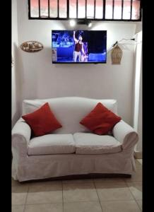 Sofá blanco con almohadas rojas y TV en la pared en Bruna Departamentos en San Fernando del Valle de Catamarca