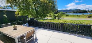 a patio with a wooden table and a fence at Perfect Lakeside Summer House in Rotorua