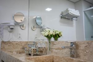 um lavatório de casa de banho com um vaso de flores e espelhos em Sofistic Hotel em Itapema