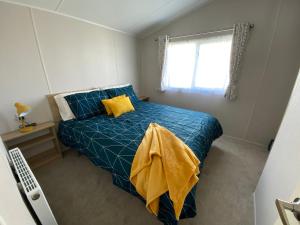 a bedroom with a blue bed with yellow pillows and a window at VerbZen Holiday Caravan at St Osyth Beach, Clacton-on-Sea by Verb Holidays in Saint Osyth +7 photos