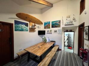 Habitación con mesa de madera y tabla de surf en la pared. en Lands End Hostel and B&B en Sennen