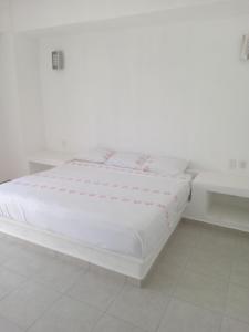 ein weißes Bett in einem Zimmer mit zwei Tischen in der Unterkunft Hotel Ixtazihua JP in Zihuatanejo + 2 Fotos