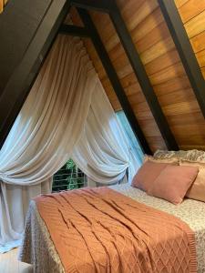 Bett in einem Zimmer mit weißen Vorhängen in der Unterkunft Chalé Romântico com cachoeira in Witmarsum