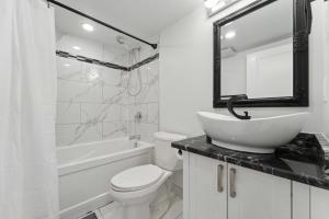 a white bathroom with a sink and a toilet and a tub at Modern 3BR Suites in Ottawa