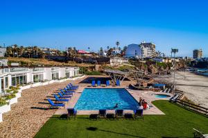 a swimming pool with people sitting in chairs next to a beach at Villa Ambar 55 - Playa Arcangel in Rosarito