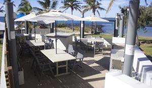 a row of tables and chairs with umbrellas and the ocean at Bargara Shoreline Apartments in Bargara