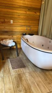 a white bath tub in a room with a wooden wall at Chalés Canto da Serra in Monte Verde