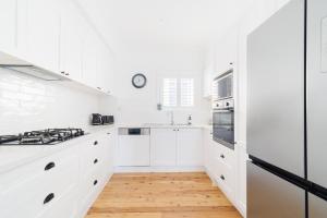 a white kitchen with white cabinets and wood floors at La Villette sleeps 9 fireplace BBQ Pet Friendly in Katoomba
