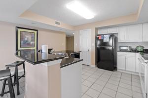 a kitchen with a black refrigerator and white cabinets at Yacht Club Villas #1-701 condo in Myrtle Beach