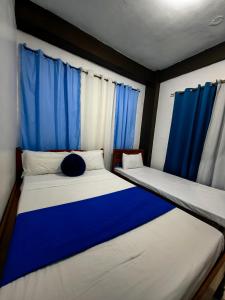 two beds in a room with blue curtains at DGA Traveler's Inn in Coron