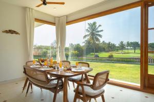 a dining room with a table and chairs and a large window at SaffronStays Niranta- Villa in Golfshire, Nandi Hills in Bangalore