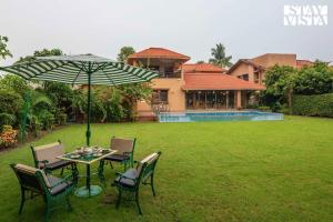 a table and chairs with an umbrella in a yard at StayVista's Ishva Bungalow - Massive Pool, Sprawling Lawn & Indoor-Outdoor Games in kolkata