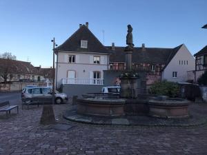 una fuente frente a un edificio con una estatua en * La Petite Alsacienne *, en Ammerschwihr
