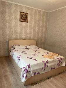ein Schlafzimmer mit einem Bett mit lila Blumen darauf in der Unterkunft Маринад in Petropawlowsk