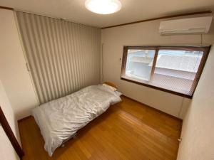 a small room with a bed and a window at ゲストハウスすまいるさん in Iba