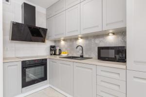 a kitchen with white cabinets and a sink and a microwave at Elegant Apartment Na Wydmach with Balcony and Parking by Renters in Międzywodzie