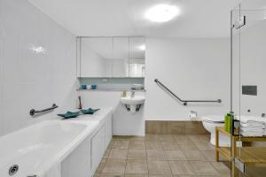 a white bathroom with a tub and a sink at Iluka Resort Apartments Palm Beach in Palm Beach