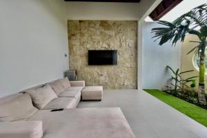 a living room with a couch and a tv on a wall at Belvilla 93824 Villa Nesa Near Titi Batu Club Ubud in Ubud