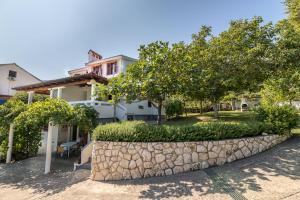 a house with a stone retaining wall and trees at Apartments Janko Zarok in Baška