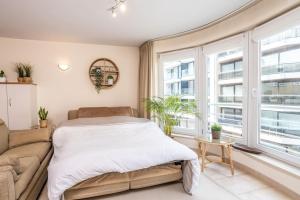 a bedroom with a bed and a couch and windows at Top studio Knokke bij zeedijk! in Knokke-Heist