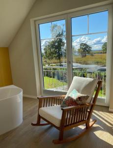 einen Schaukelstuhl in einem Zimmer mit einem großen Fenster in der Unterkunft Ferienhaus Am Hafen 11 Altwarp mit Sauna, Kamin und Wasserblick in Altwarp