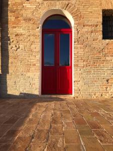 uma porta vermelha num edifício de tijolos com um arco em B&B San Nicola em Porchia