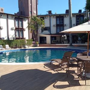 a swimming pool with chairs and a table and an umbrella at Hotel Damen in Foz do Iguaçu
